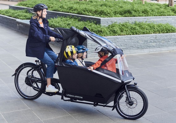 Une mère sur un vélo électrique cargo transporte ses trois enfants