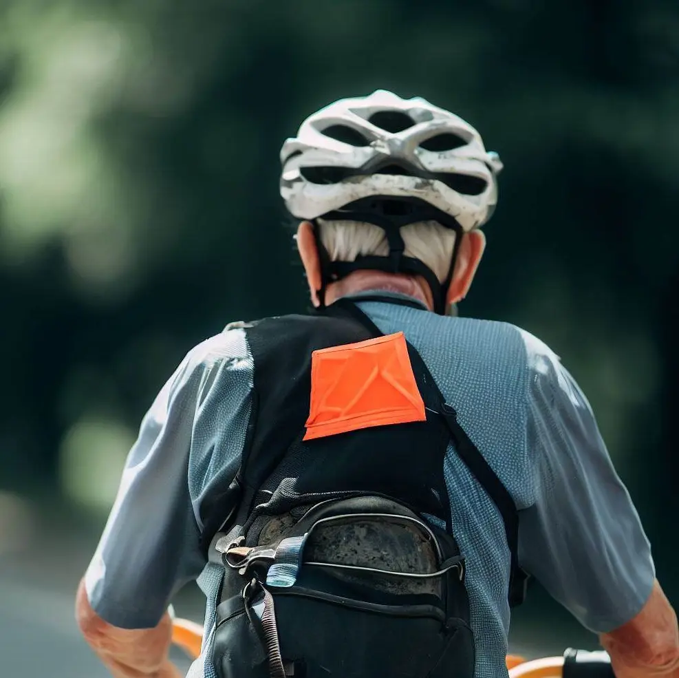 Un cycliste aux cheveux blancs de dos, portant un casque de protection et un sac réfléchissant 